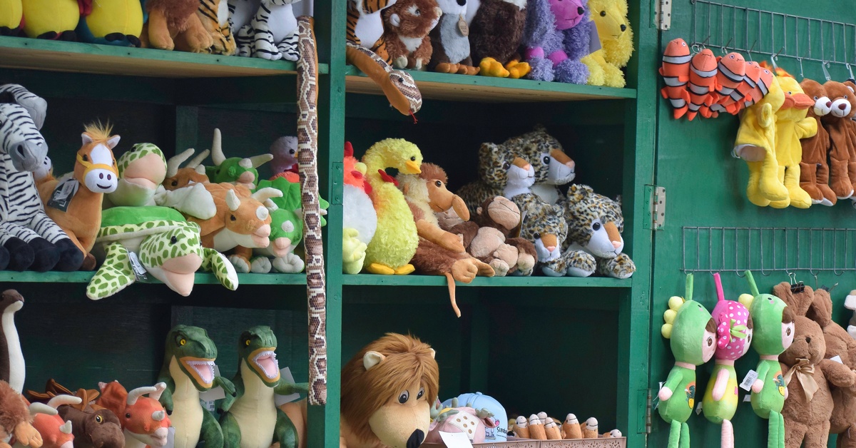 Stuffed animals sitting on green shelves like dinosaurs and cheetahs. Some stuffed animals are hanging on a nearby wall.