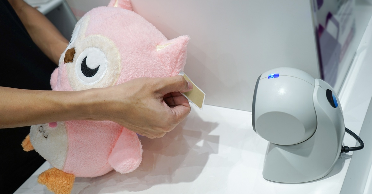 A person using a scanner at a checkout area. They are holding out the tag of a stuffed animal in front of the scanner.