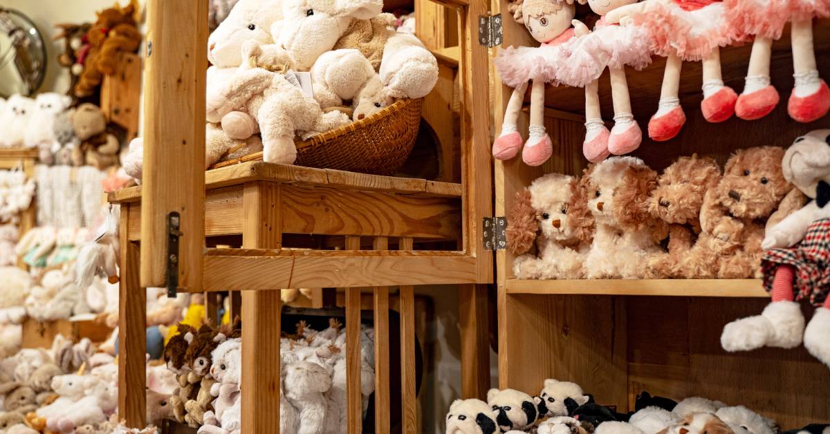 Multiple wooden shelves of plush toys with different designs. Some toys are sheep, dogs, and penguins.
