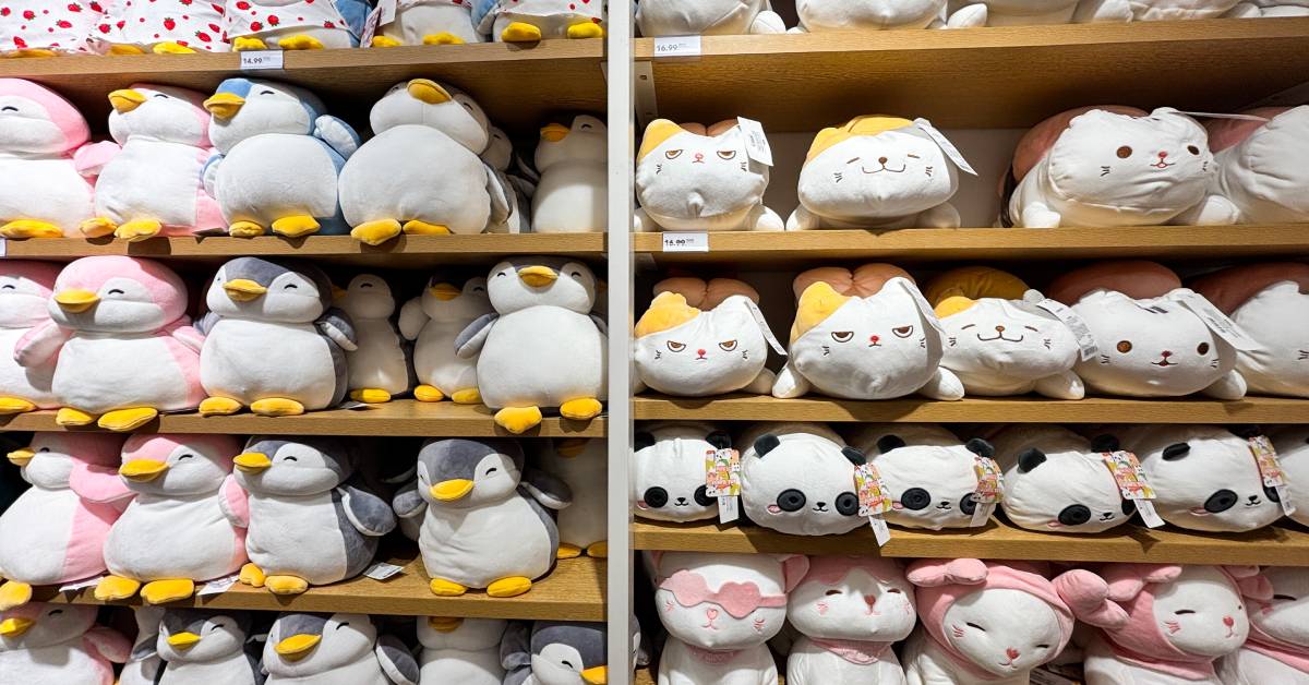 Bright lights over tall wooden shelving. Plush cats and penguins with different expressions sit on the shelves.