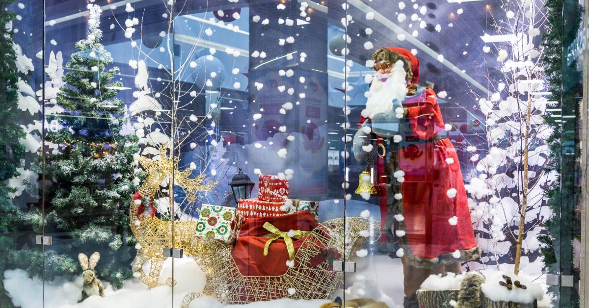A window display showcasing a Christmas tree and Santa Claus decorations with fake snow on the ground.